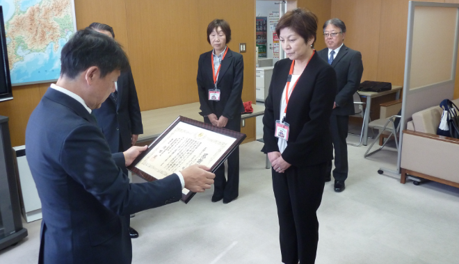 贈呈式で職員が女性に賞状を授与する様子